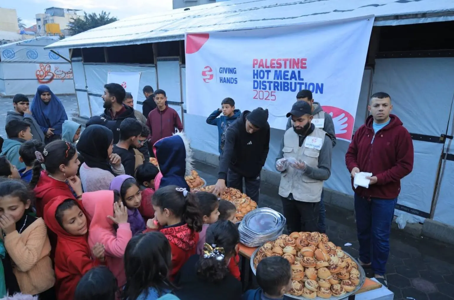 Crowd of children and families receiving hot meals during Palestine Hot Meal Distribution by Giving Hands كندا in 2025