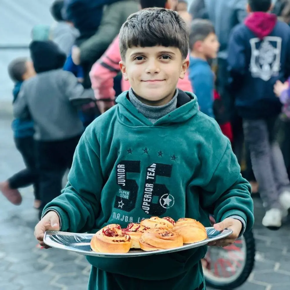 Child holding a tray of fresh pastries during a food distribution event in Palestine by Giving Hands كندا