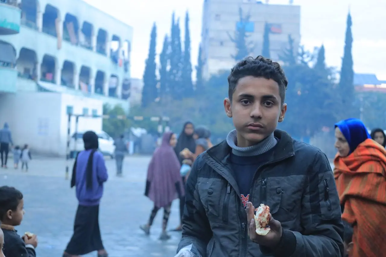 Young person holding bread in an outdoor area during a food aid distribution in Palestine by Giving Hands كندا