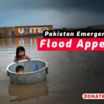 Children in a metal tub in floodwater with Pakistan Flood Appeal banner.